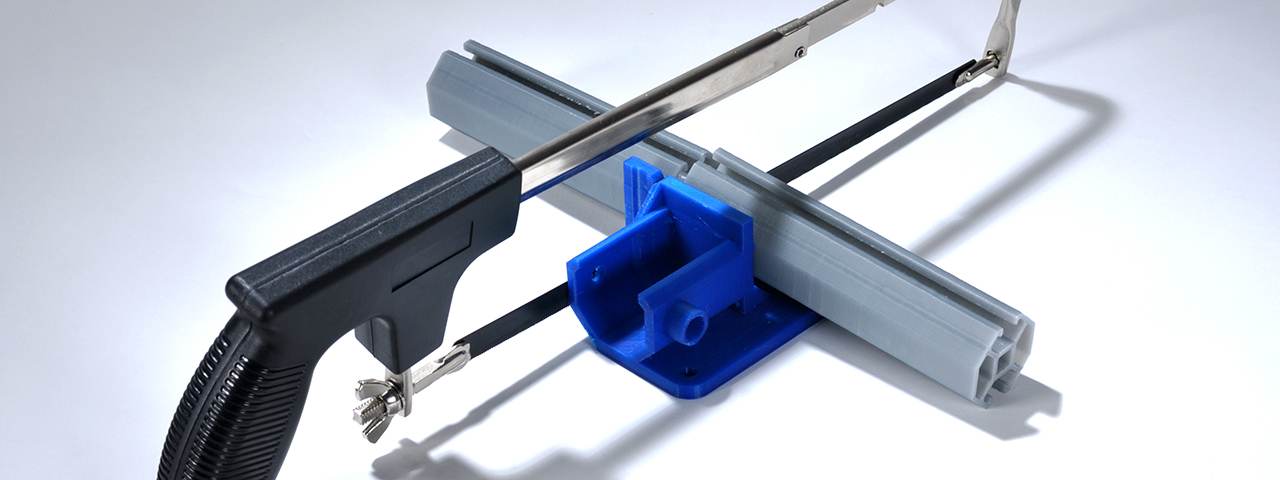 A blue MakeWiths clip holding a hacksaw frame to a gray extrusion